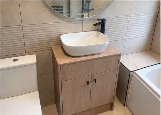 Bathroom with a white countertop basin on an oak-effect vanity unit, matt black tap, fluted beige wall tiles and a round mirror above