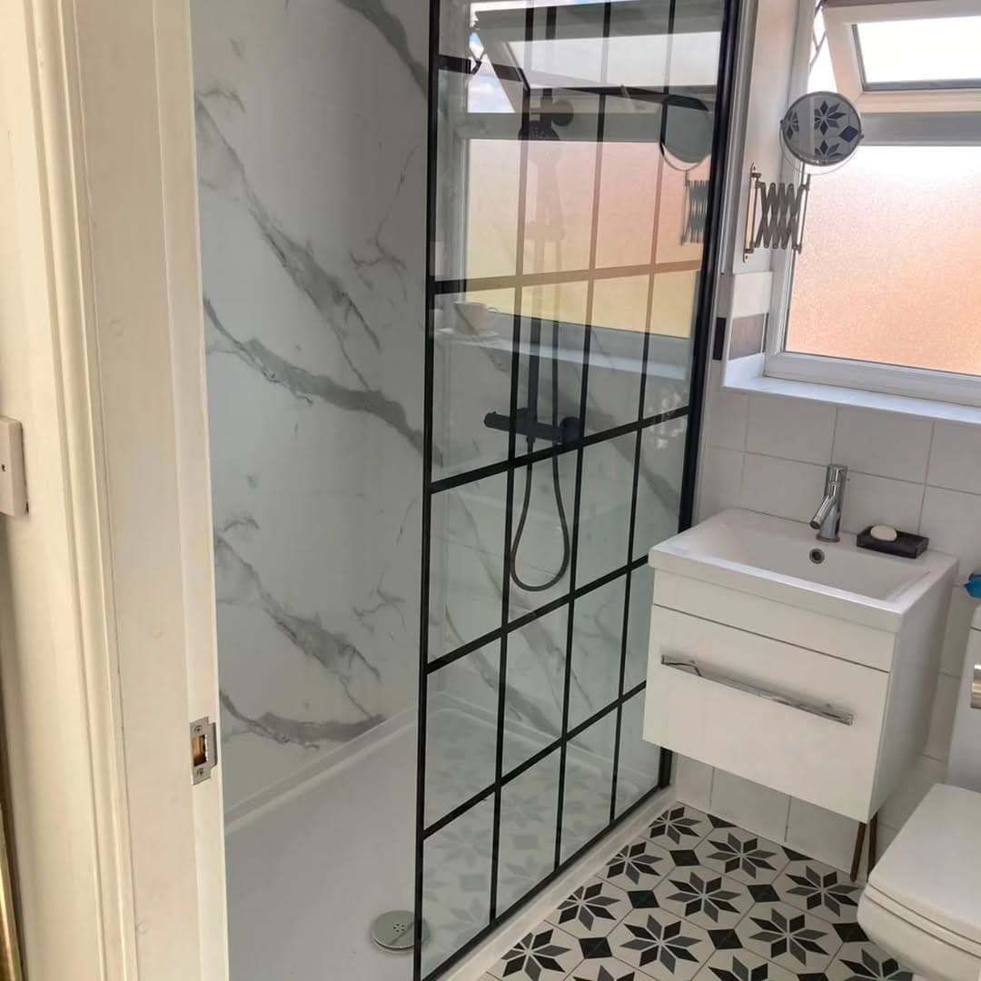 Modern bathroom with a level-access walk-in shower behind a black crittall-style glass screen, marble-effect wall panels and a patterned floor
