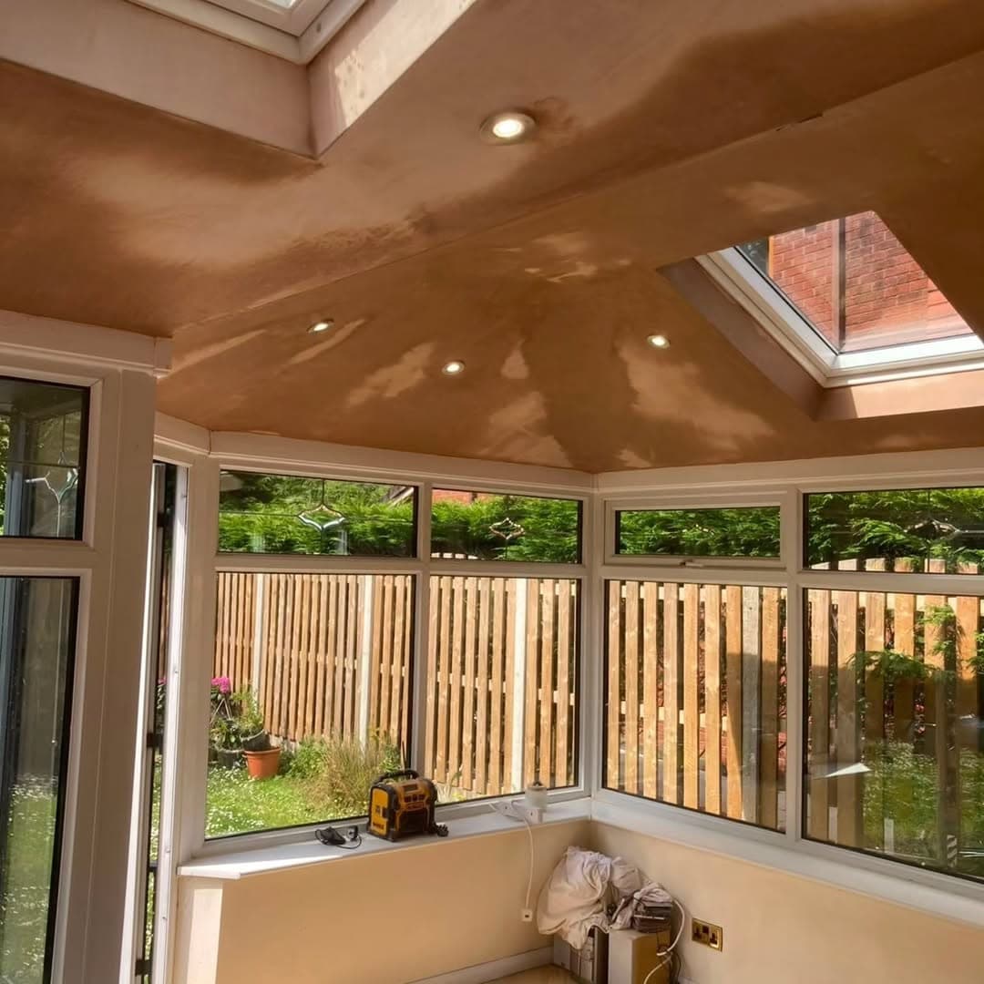Interior of a converted conservatory with a plastered ceiling, recessed spotlights and a roof window, looking out over the garden