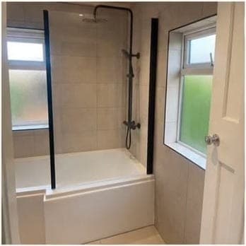 Bath with a black-framed glass shower screen beside an obscured-glass window, in a beige-tiled bathroom