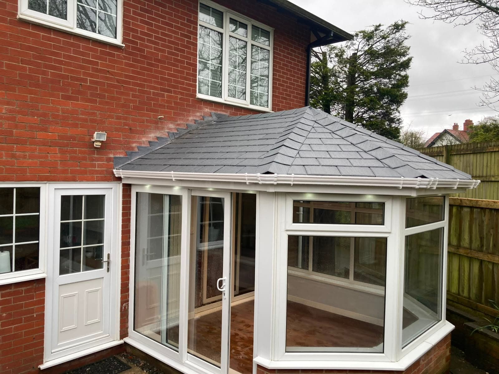 Red brick house with a white uPVC conservatory carrying a new grey tiled warm roof