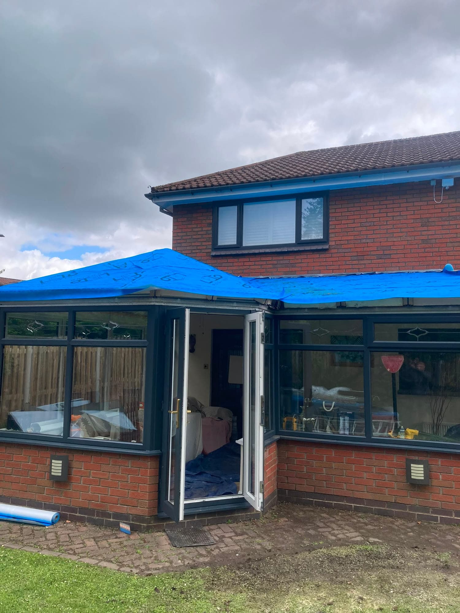 A conservatory roof conversion in progress, with the structure sheeted over in blue tarpaulin while the new roof goes on