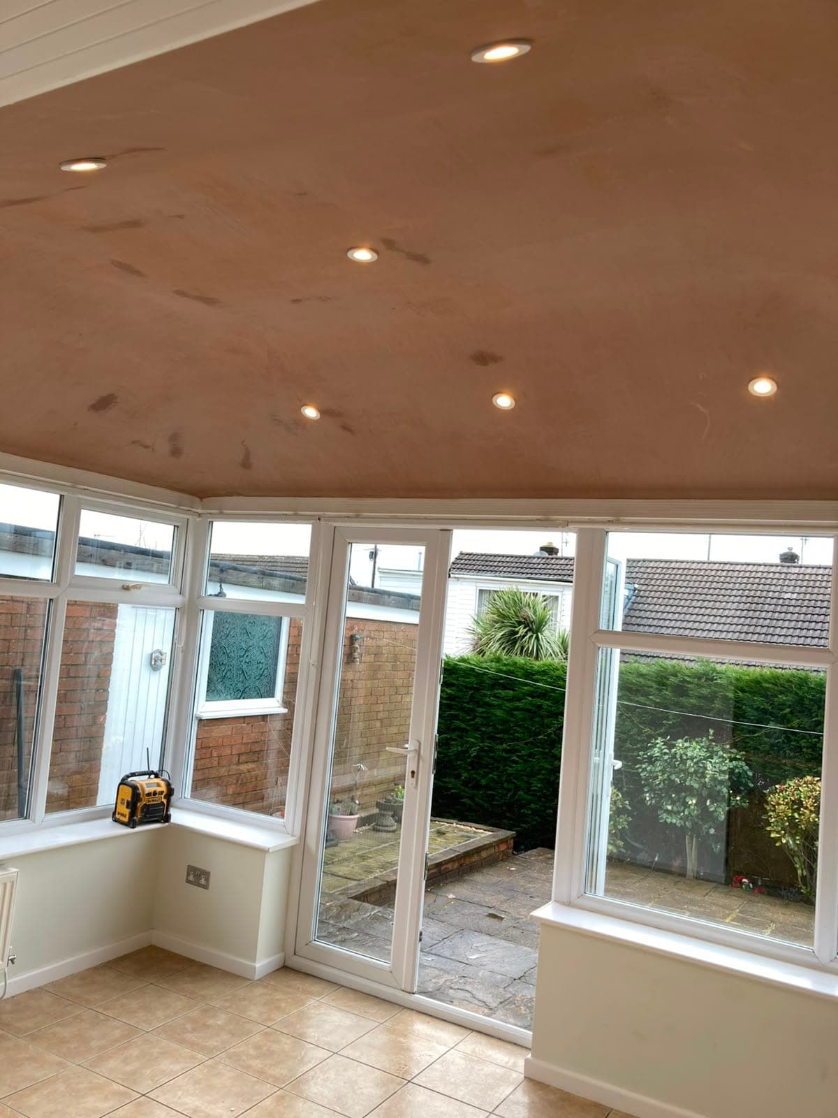Inside a converted conservatory with white French doors onto the garden and a newly plastered ceiling