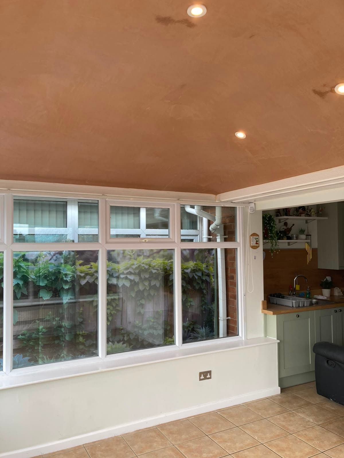 Converted conservatory interior with a plastered ceiling and recessed lighting, opening off the kitchen