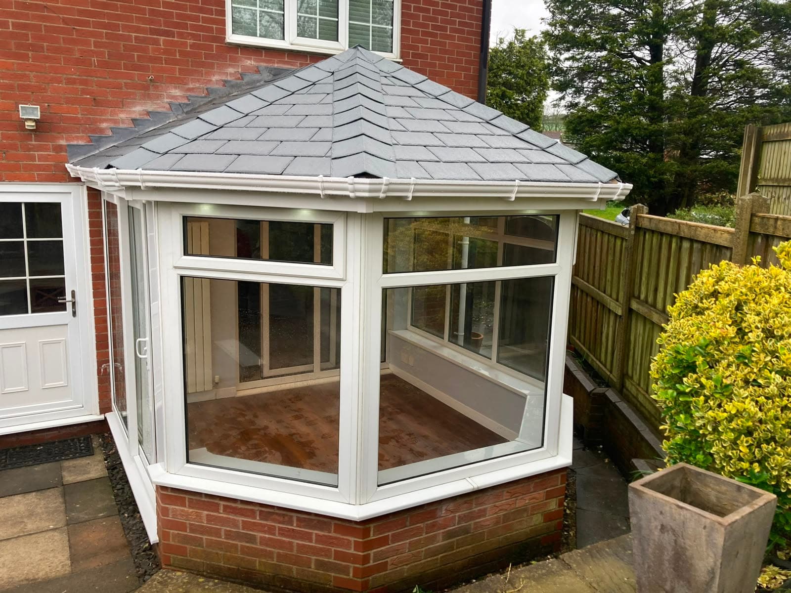 White uPVC conservatory with a new grey tiled warm roof sitting on a red brick dwarf wall